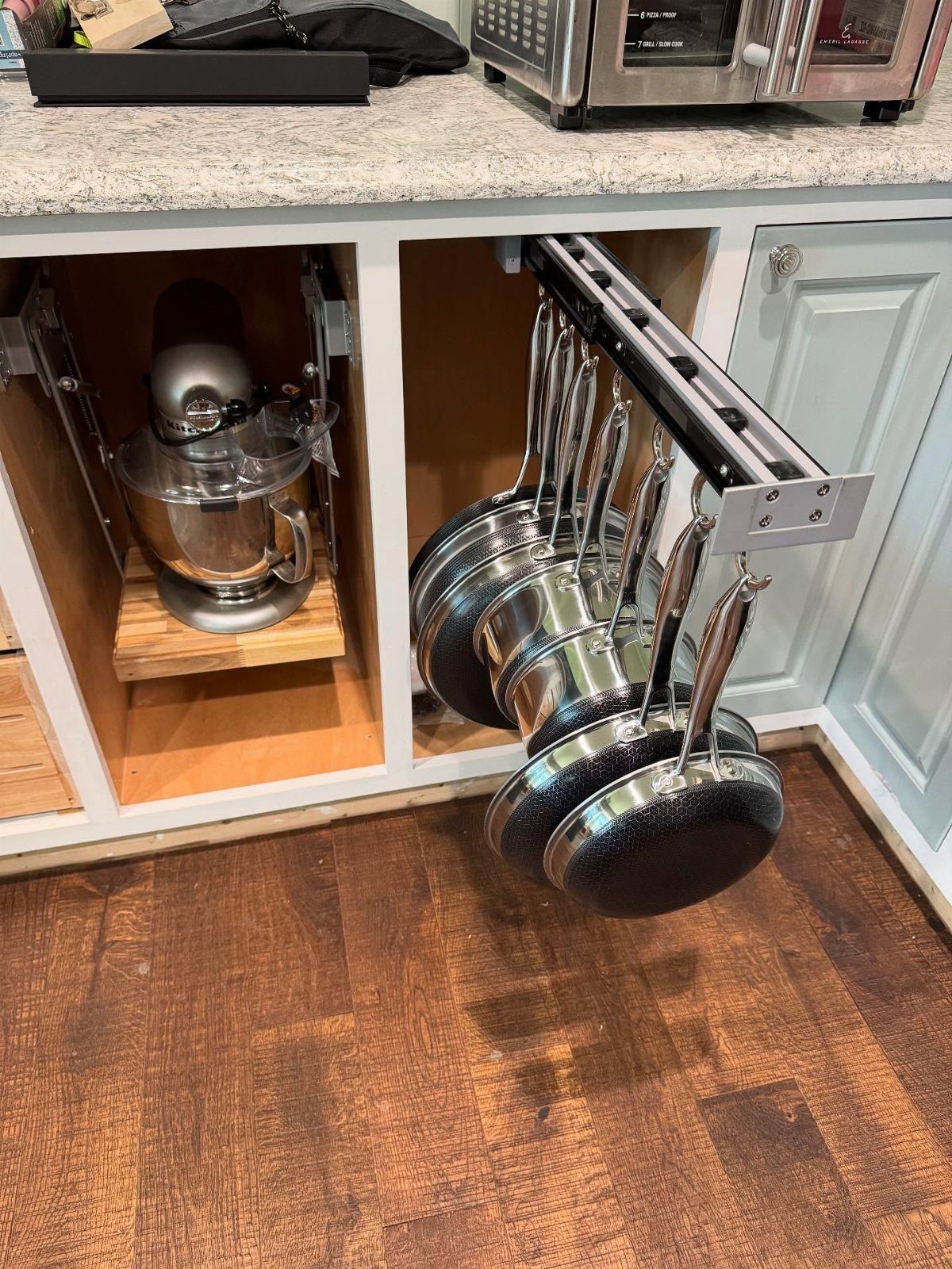 A pull-out kitchen cabinet drawer containing several hanging black frying pans and pots.