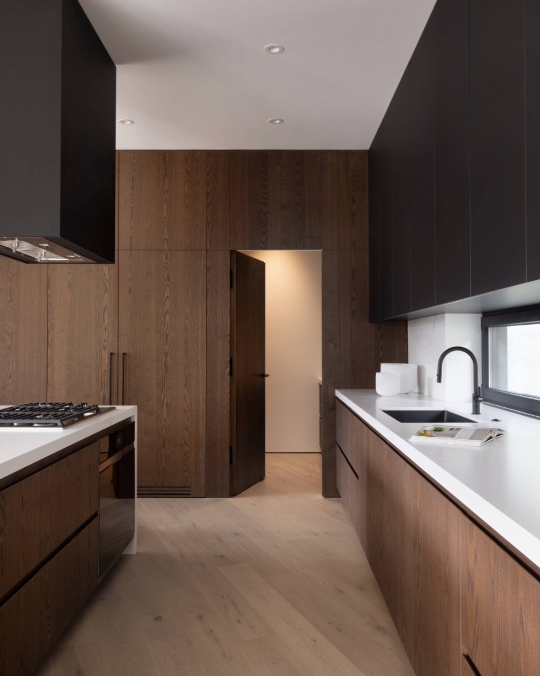 Modern kitchen with dark wood paneled walls and a seamless flush pantry door.
