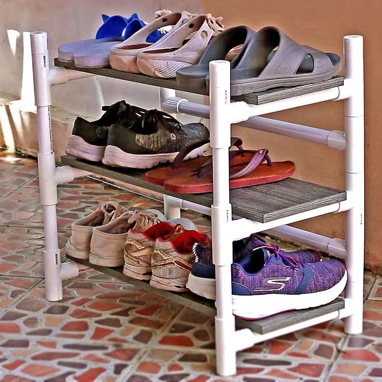 A three-tier shoe rack made from white PVC pipes and wooden planks holding various footwear.