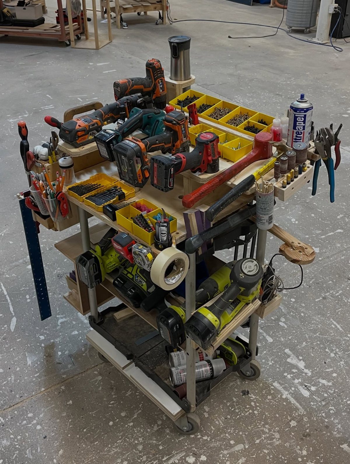 A wooden mobile tool cart filled with various power tools and organizers in a workshop.