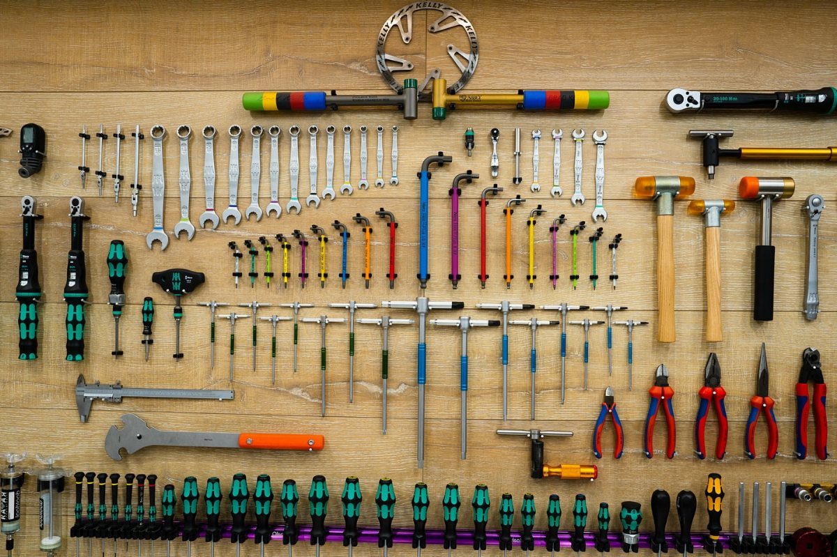 Various hand tools organized in neat rows on a light brown wooden surface.